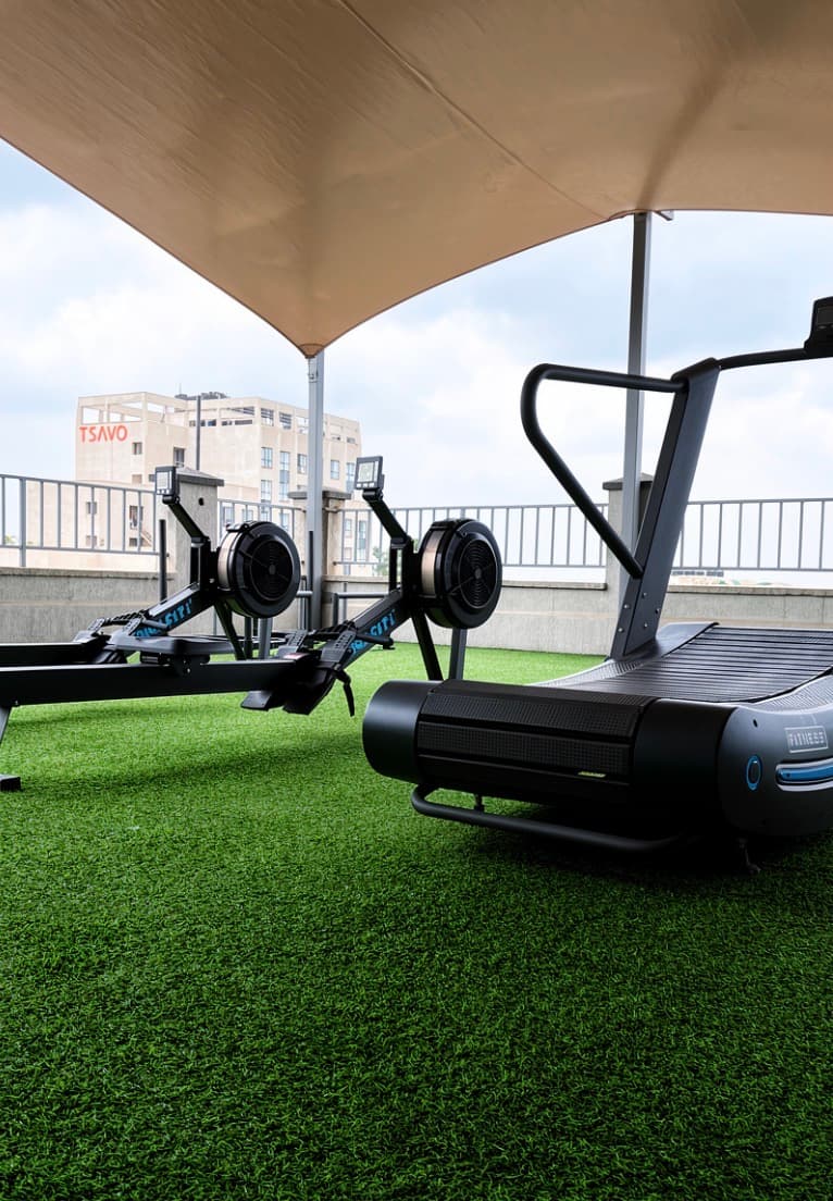 Rowers and a curved treadmill on the rooftop turf, Nairobi skyline behind